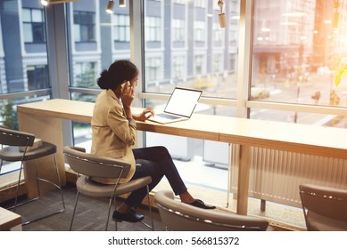 Young Afroamerican Executive Making Remote Job Being In Business Trip Sitting At Table In Coworking Space Talking On The Phone With Entrepreneur Using Laptop Computer With Mock Up Screen With Wifi