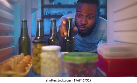 Young Afro-american Guy Opening Refrigerator And Taking Cool Beer Bottle Holding Bowl With Popcorn Preparing To Watch Sport Game Spending Evening At Home