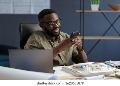 Young Afro-American man using smartphone and smiling. Happy businessman using mobile phone apps, texting message, browsing internet, looking at smartphone. Young people working with mobile devices. - Powered by Shutterstock