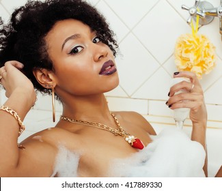 young afro-american teen girl laying in bath with foam, wearing swag jewelry flawless, making selfie, modern lifestyle concept