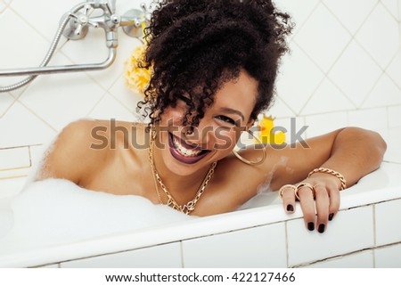 young afro-american teen girl laying in bath with foam, wearing swag jewelry flawless, making selfie, modern lifestyle people concept