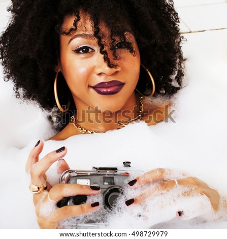 young afro-american teen girl laying in bath with foam, wearing 