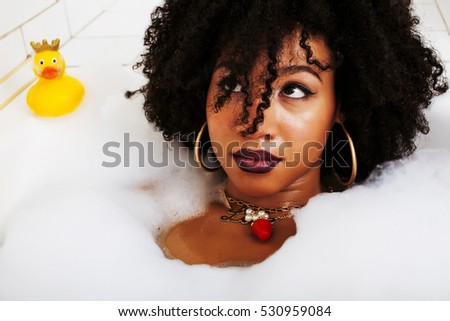 young afro-american teen girl laying in bath with foam, wearing 