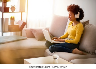 Young afro-american Woman drinking water and surfing the net on the sofa at home. Young woman working from home office. Freelancer using laptop, phone and the Internet. Workplace in living room - Powered by Shutterstock - Get 15% off with code: PIKWIZARD15