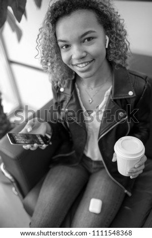 Young afro-american woman sitting in waiting room and using smartphone.