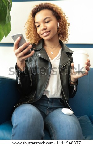 Young afro-american woman sitting in waiting room and using smartphone.