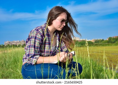 young agronomist brunette woman crouching on the ground and checks the quality of the soil and marks data on her notebook