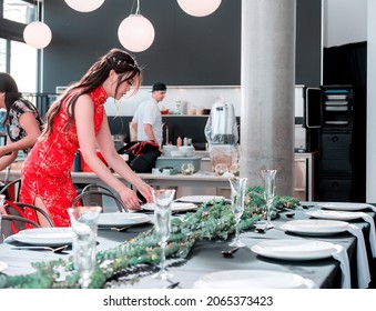 Young Aian Woman in red traditional Chinese dress serving plates and glasses on elegant table. People working in restaurant. Woman wedding designer arrange table setting