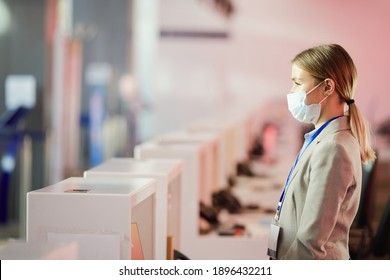 Young Airport Worker In Protective Mask Standing At Reception Desk And Working