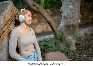 Young albino african american woman with headphones is enjoying music while leaning against a tree trunk in a park, embracing the tranquility of nature - Powered by Shutterstock