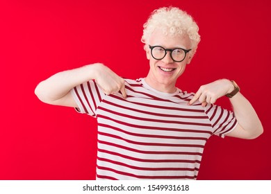 Young albino blond man wearing striped t-shirt and glasses over isolated red background looking confident with smile on face, pointing oneself with fingers proud and happy. - Powered by Shutterstock