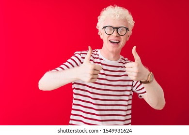 Young albino blond man wearing striped t-shirt and glasses over isolated red background success sign doing positive gesture with hand, thumbs up smiling and happy. Cheerful expression - Powered by Shutterstock