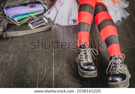Young alternative girl sitting on the black floor with a school bag, smartphone, sunglasses and headphones. Education, alternative life style, modern life concept