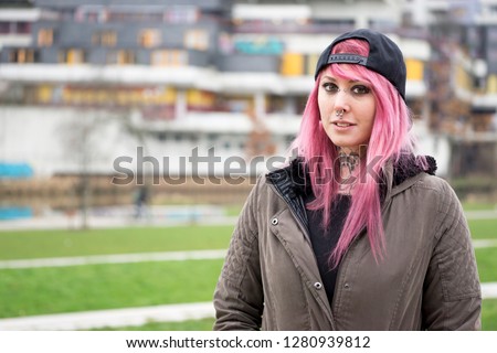 young alternative woman with pink hair standing in front of run-down housing estate                       