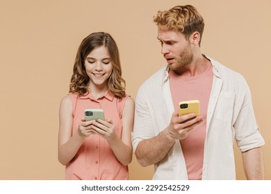 Young amazed confused azed parent man with child teen girl wear casual pastel clothes. Daddy little kid daughter using mobile cell phone isolated on beige background. Father's Day Love family concept