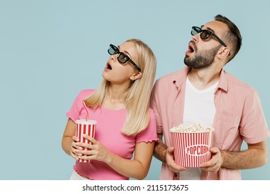 Young Amazed Couple Man Woman Friends In 3d Glasses Watch Movie Film Hold Bucket Of Popcorn Cup Of Soda Pop Looking Aside Isolated On Plain Blue Background Studio People Emotions In Cinema Concept.