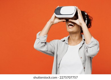 Young amazed fun happy smiling woman of African American ethnicity she wears grey shirt headband watching in vr headset pc gadget isolated on plain orange background studio. People lifestyle concept - Powered by Shutterstock