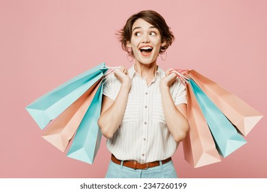 Young amazed surprised shocked woman wear casual clothes hold shopping paper package bags look aside on area isolated on plain pastel pink color background studio. Black Friday sale buy day concept