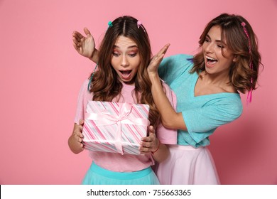 Young Amazed Woman Holding Present While Celebrating Birthday With Her Female Friend, Isolated Over Pink Background