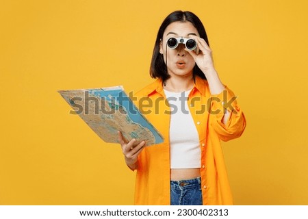 Young amazed woman wear summer casual clothes hold in hand map use binoculars isolated on plain yellow background. Tourist travel abroad in free spare time rest getaway Air flight trip journey concept