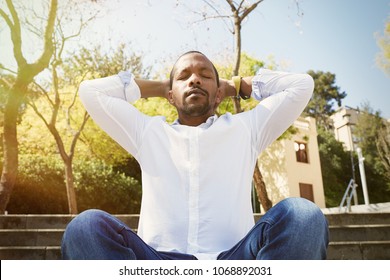 Young American African Businessman In White Shirt Put His Hands On His Head And Taking A Deep Breath Outside Corporate Office.Business Yoga And Stress Free Environment.Peace Of Mind Concept