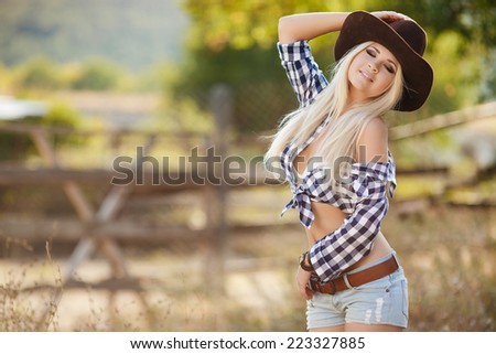 Young american cowgirl woman portrait outdoors. Beautiful natural woman saying hello looking at camera touching cowboy hat. girl in her twenties outdoor in nature.