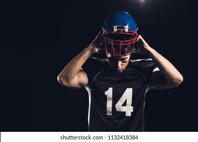 Young American Football Player Putting On Helmet Isolated On Black