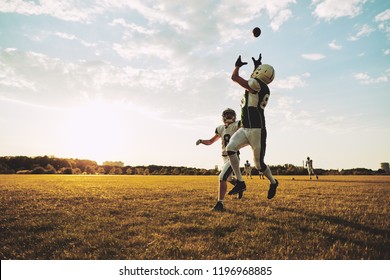 Young American football player receiving a pass during team practice on a football field in the afternoon - Powered by Shutterstock