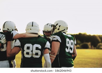 Young American Football Players Standing In A Huddle Together On A Sports Field During An Afternoon Team Practice