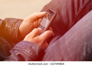 Young American Man Holding A Mobile Smartphone In His Hands While Sitting In An Easy Chair