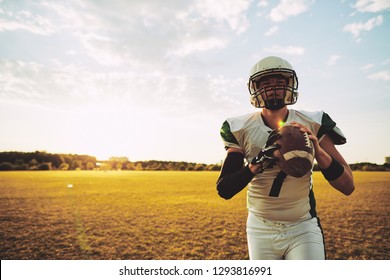 Young American quarterback holding a football while standing alone on a sports field in the late afternoon - Powered by Shutterstock