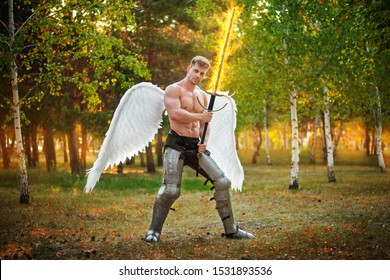 A young angel, a bodybuilder in plate armor on his legs with wings behind his back, holds in his hands a fiery two-handed sword.