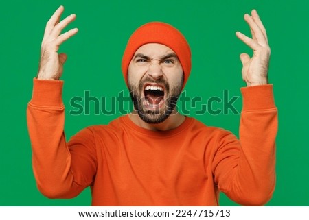 Young angry furious sad indignant caucasian man 20s wear orange sweatshirt hat spread hands scream shout abusing swearing isolated on plain green background studio portrait. People lifestyle concept
