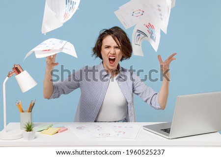 Young angry indignant sad director employee business woman in casual shirt sit work at white office desk with pc laptop throwing up paper account documents isolated on pastel blue background studio