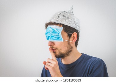 Young angry man with face mask over the eyes and aluminum hat is doing a psst! gesture