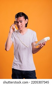 Young Angry Man Talking On Landline Phone. Irritated Asian Teenager Shouting, Holding Retro Telephone, Person With Annoyed Facial Expression Having Conversation, Answering Call