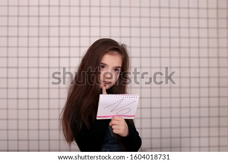 young angry playful girl of eight years with long hair in a black turtleneck and jeans sundress with the sign "NO"