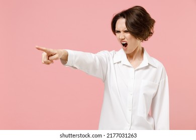 Young angry serious strict employee business woman corporate lawyer in classic formal white shirt work in office point index finger aside scream shout do it isolated on pastel pink color background
