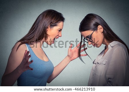 Young angry woman abusing screaming at another scared nerdy one in glasses isolated on gray background