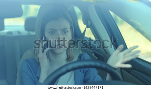 Young angry woman driver talking by phone while\
driving a car serious sunset sunlight communication adult cellphone\
female automobile dangerous connection road sitting smartphone\
texting slow motion