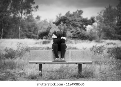 Young Anonymous Depressed Woman Sitting Alone On A Bench With Arm Crossed In Front Of Her Face. Monochrome Portrait.