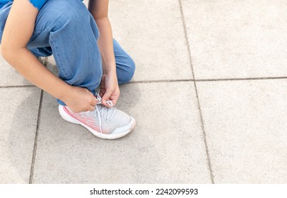 Young anonymous girl, elementary school age child tying her shoe, shoelaces. Child tying shoes outdoors hands closeup, detail, copy space. Generic modern kids footwear simple concept, one person - Powered by Shutterstock