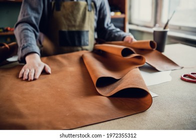 A young apprentice in a boot workshop prepares leather for further use on a large table - Powered by Shutterstock