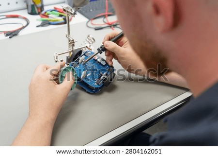 A young apprentice re-soldering on a PCB or circuit board and fixing an RC car