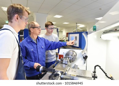 young apprentices in technical vocational training are taught by older trainers on a cnc lathes machine - Shutterstock ID 1015846945