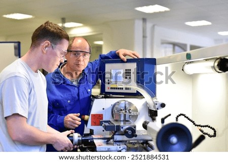 young apprentices in technical vocational training are taught by older trainers on a cnc lathes machine