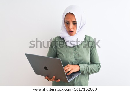 Young Arab business woman wearing hijab using laptop over isolated background scared in shock with a surprise face, afraid and excited with fear expression