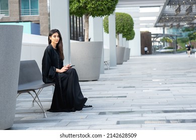 Young Arab Businesswoman Wearing Abaya Sitting Carrying Mobile Phone. Woman Looking Emirati Or Saudi Outdoors Posing