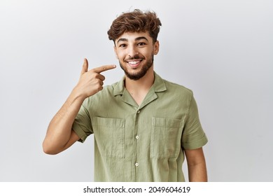 Young Arab Doctor Man Standing Over Isolated Background Pointing With Hand Finger To Face And Nose, Smiling Cheerful. Beauty Concept 