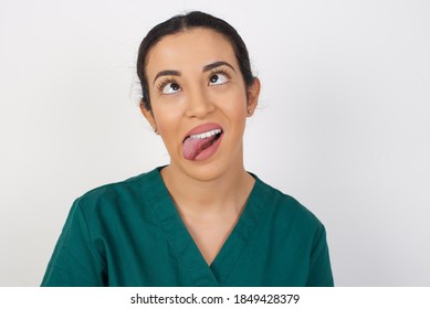 Young Arab Doctor Surgeon Woman Over Isolated White Background Showing Grimace Face Crossing Eyes And Showing Tongue. Being Funny And Crazy